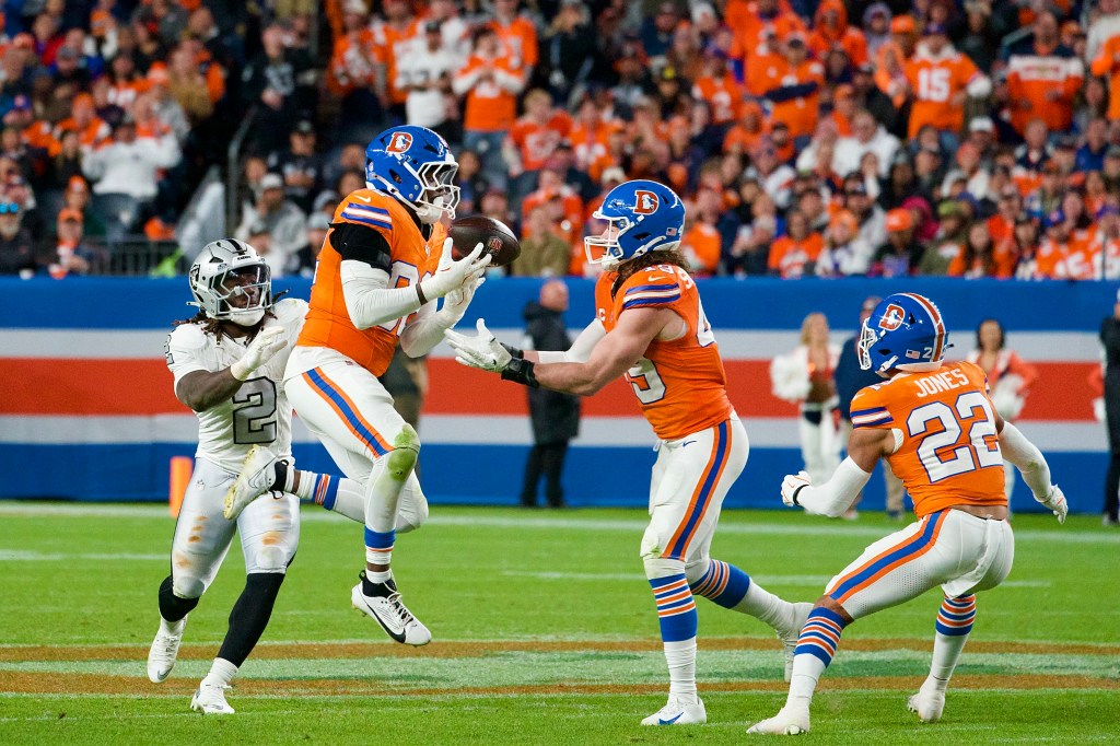 Denver Broncos linebacker Dondrea Tillman intercepts a pass against the Las Vegas Raiders at Empower Field at Mile High on Thursday Night Football, returning it upfield behind a block from Alex Singleton as the Denver defense celebrates during the team’s 10–7 win.